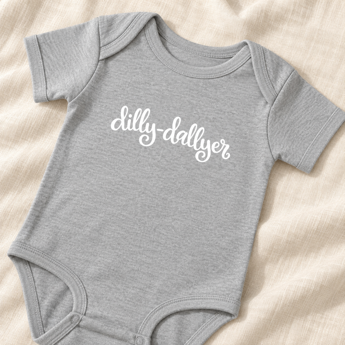 Heather gray baby bodysuit close-up showing white “dilly-dallyer” script and lap shoulders