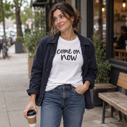 Woman wearing a white Come On Now tee with a navy jacket and jeans outside a cafe.