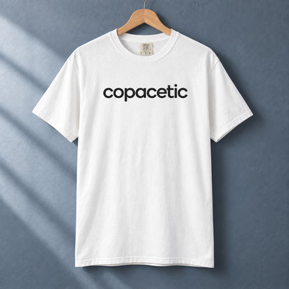 White Copacetic graphic tee on a wood hanger against a blue-gray wall.