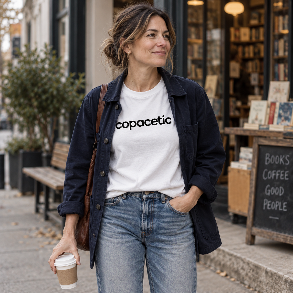 Woman wearing a white Copacetic tee with jeans and a navy jacket outside a bookstore.