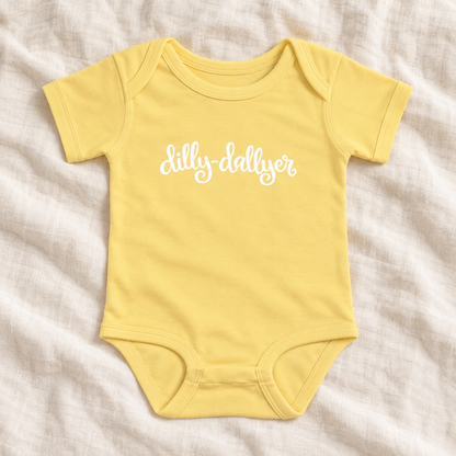 Banana baby bodysuit with white “dilly-dallyer” script, laid flat on ivory linen