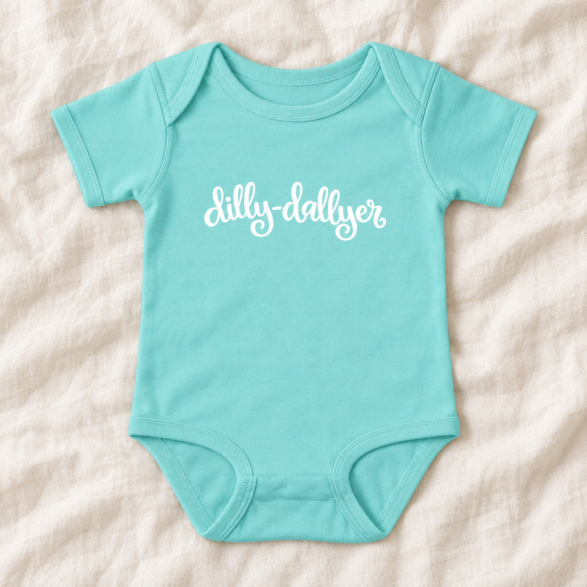 Chill baby bodysuit with white “dilly-dallyer” script, laid flat on ivory linen