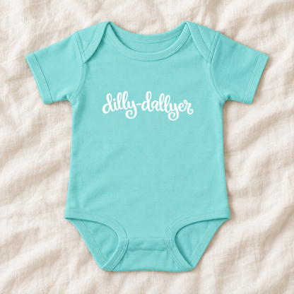 Chill baby bodysuit with white “dilly-dallyer” script, laid flat on ivory linen