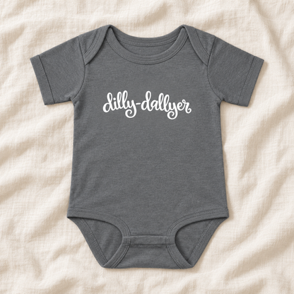 Granite Heather baby bodysuit with white “dilly-dallyer” script, laid flat on ivory linen