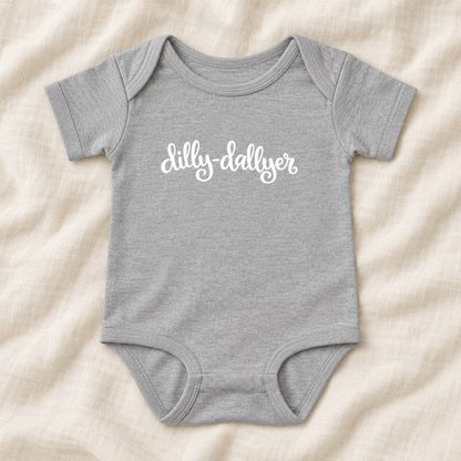 Heather baby bodysuit with white “dilly-dallyer” script, laid flat on ivory linen