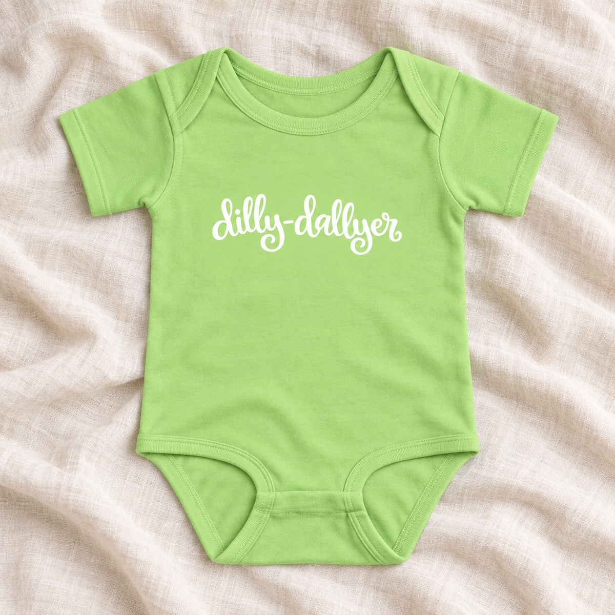 Key Lime baby bodysuit with white “dilly-dallyer” script, laid flat on ivory linen