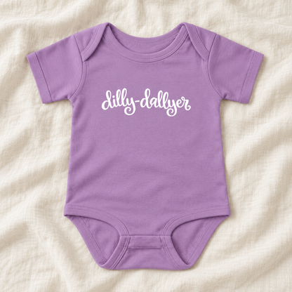 Lavender baby bodysuit with white “dilly-dallyer” script, laid flat on ivory linen
