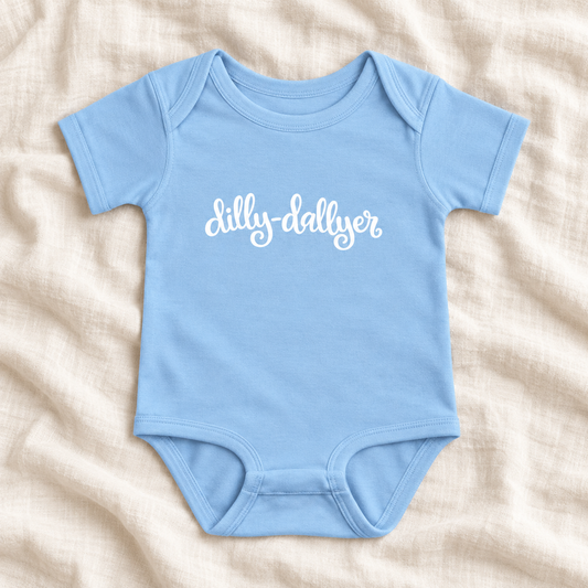 Light Blue baby bodysuit with white “dilly-dallyer” script, laid flat on ivory linen
