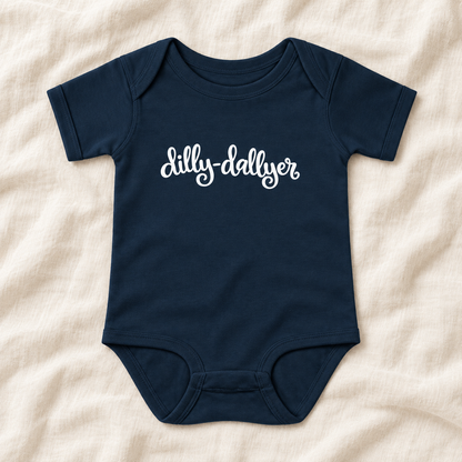 Navy baby bodysuit with white “dilly-dallyer” script, laid flat on ivory linen