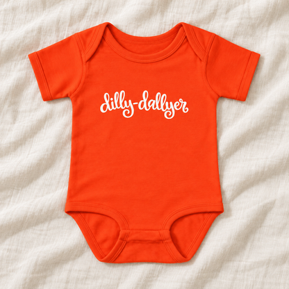 Orange baby bodysuit with white “dilly-dallyer” script, laid flat on ivory linen
