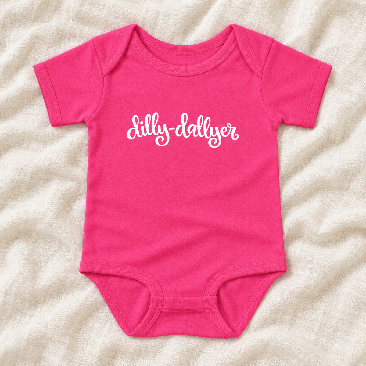 Raspberry baby bodysuit with white “dilly-dallyer” script, laid flat on ivory linen