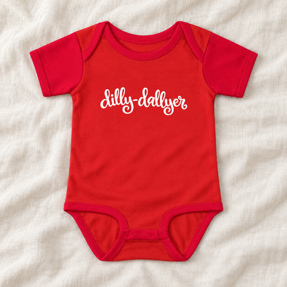 Red baby bodysuit with white “dilly-dallyer” script, laid flat on ivory linen