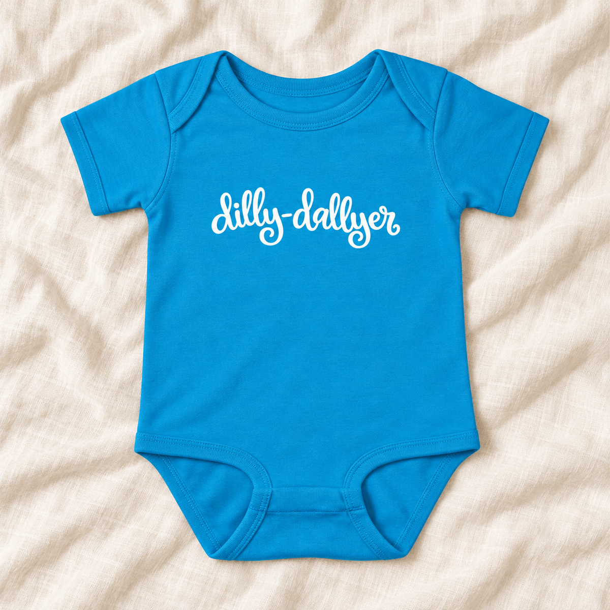 Turquoise baby bodysuit with white “dilly-dallyer” script, laid flat on ivory linen