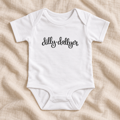 White baby bodysuit with black “dilly-dallyer” script, laid flat on ivory linen