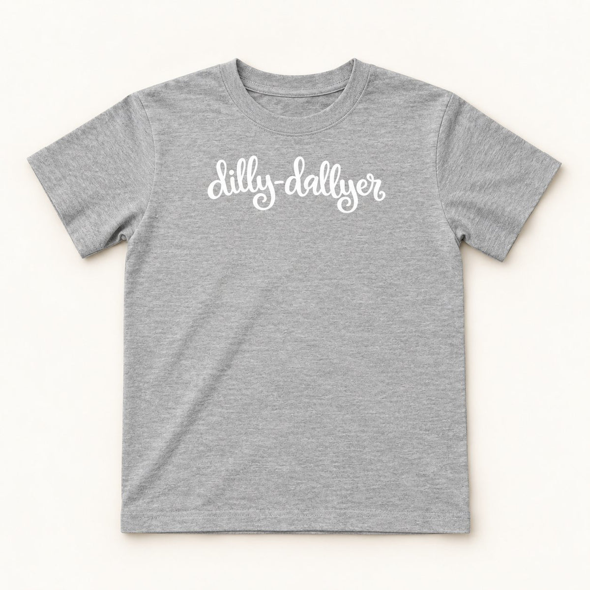 Heather Dilly-Dallyer kids tee with white script, flat on a cream background