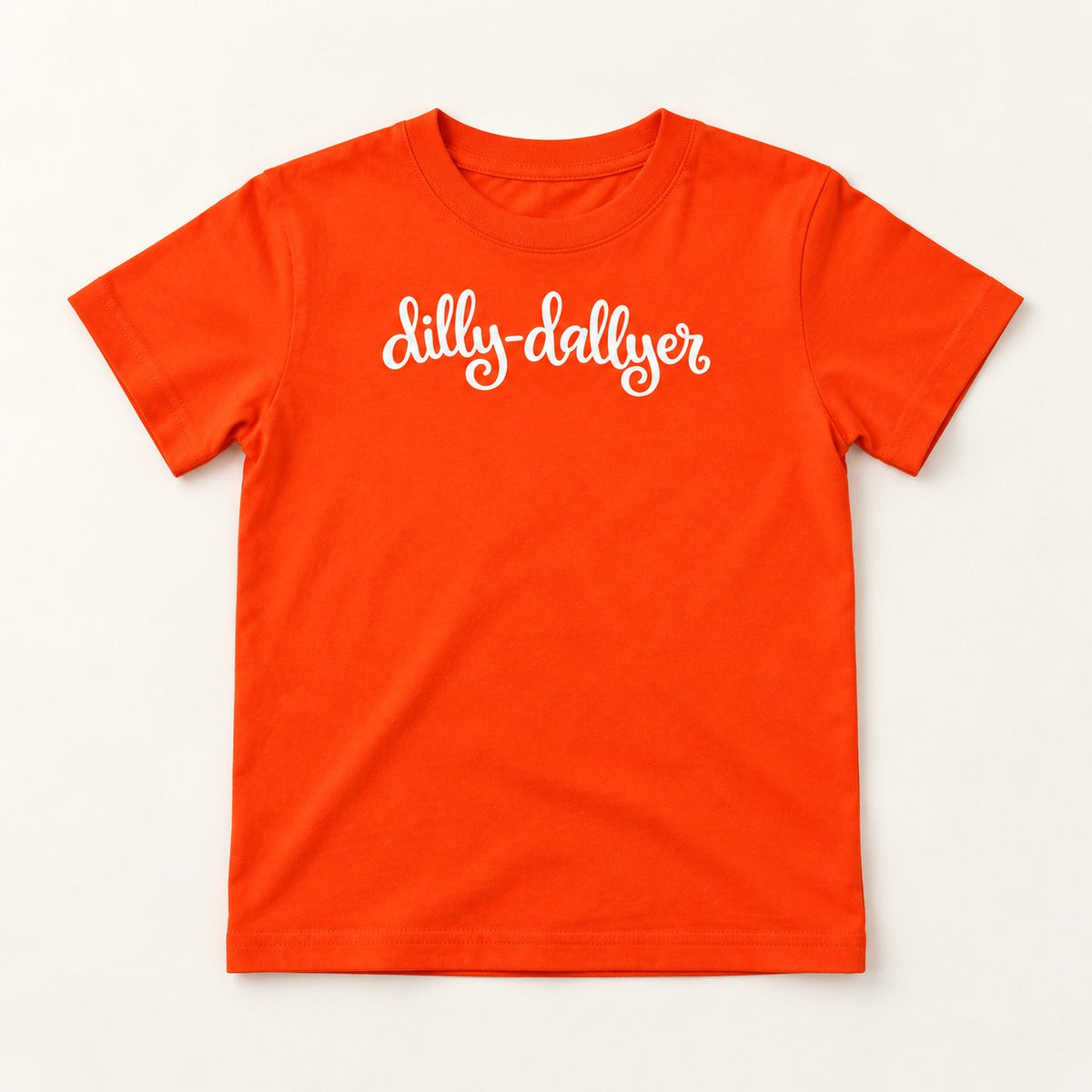 Orange Dilly-Dallyer kids tee with white script, flat on a cream background