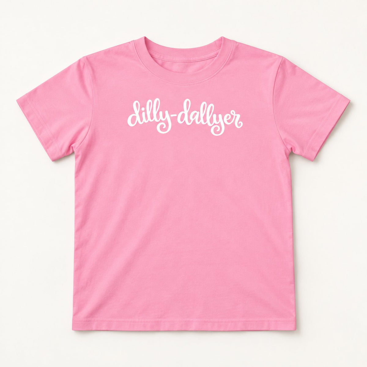 Pink Dilly-Dallyer kids tee with white script, flat on a cream background