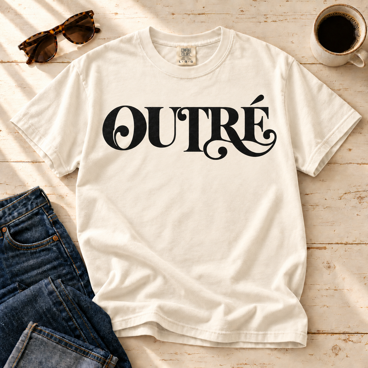 Ivory Outré tee laid flat with jeans, sunglasses, and a cup of coffee.