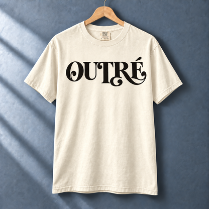 Ivory Outré tee with black flourished typography on a hanger against a blue-gray wall.